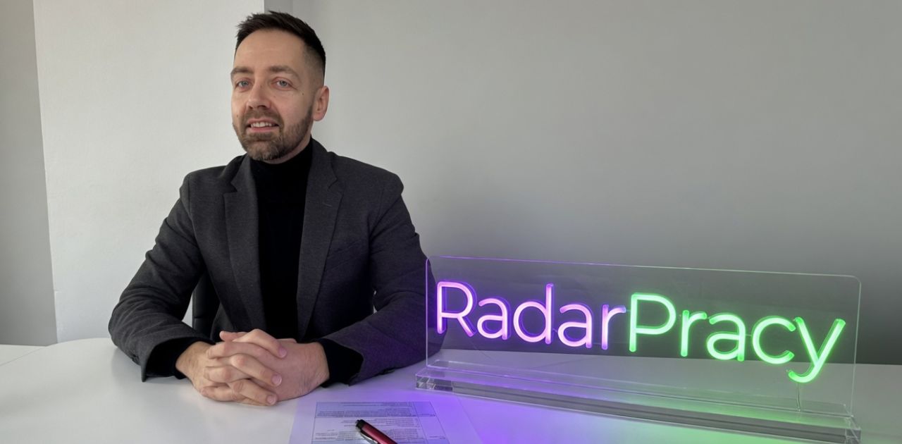 Igor Lewandowski, założyciel RadarPracy, przy neonie z logo RadarPracy